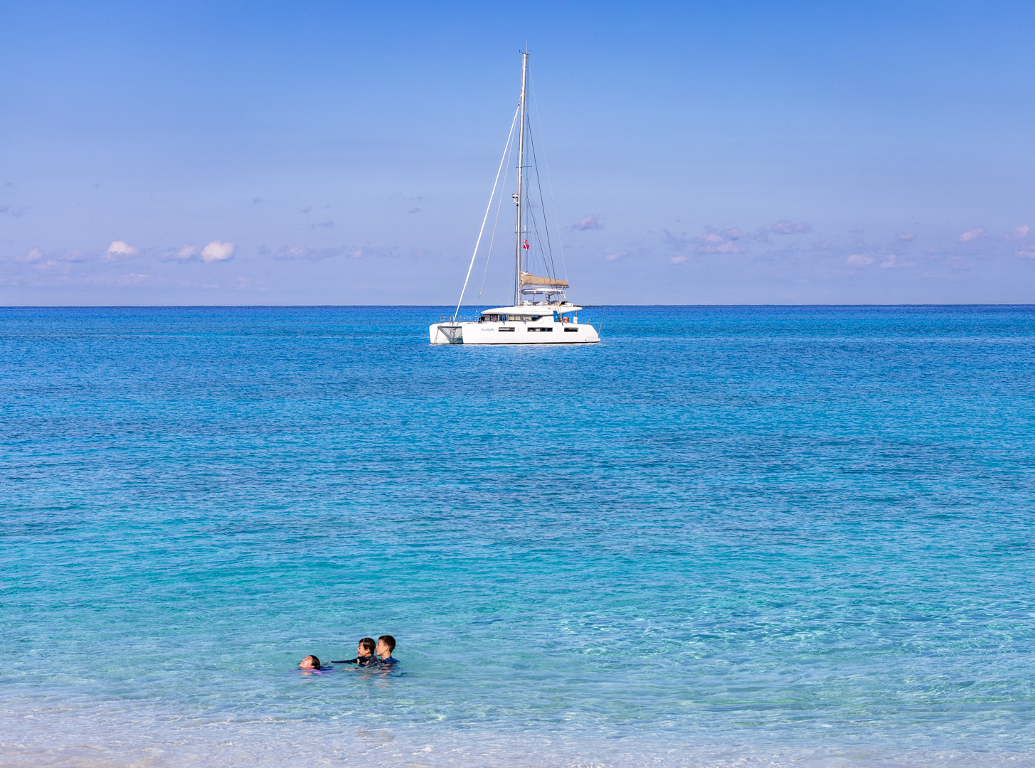 PurelyBlu anchored off an empty Exumas beach with guests swimming in the shallows