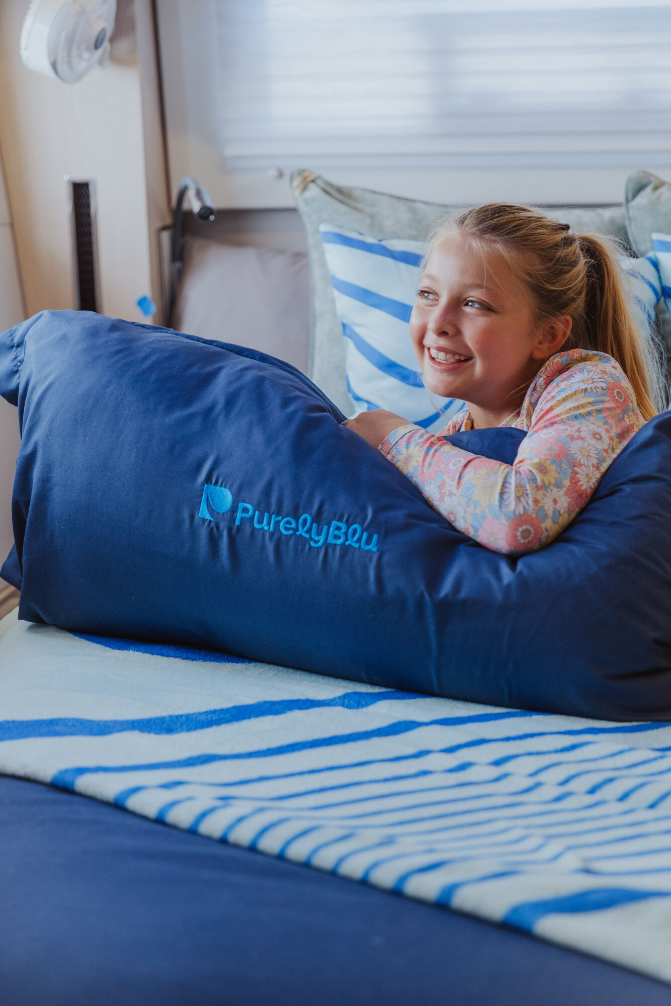 Young girl hugging PurelyBlu branded pillow with genuine smile