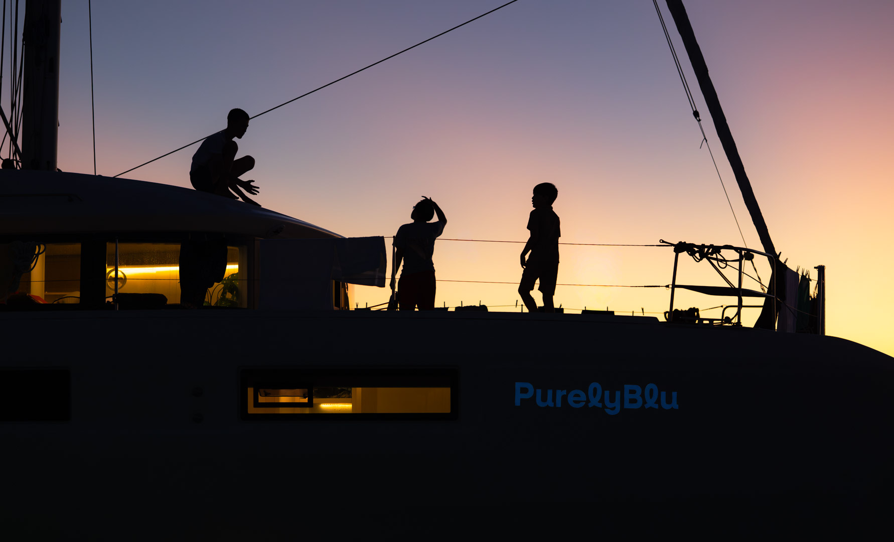Guests on deck at dusk with PurelyBlu's cabin lights glowing through the windows